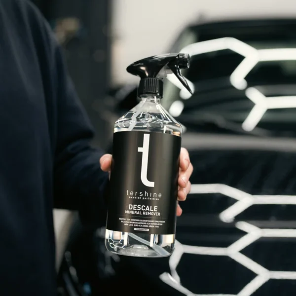 Man houdt de fles Tershine Descale vast bij een zwarte auto